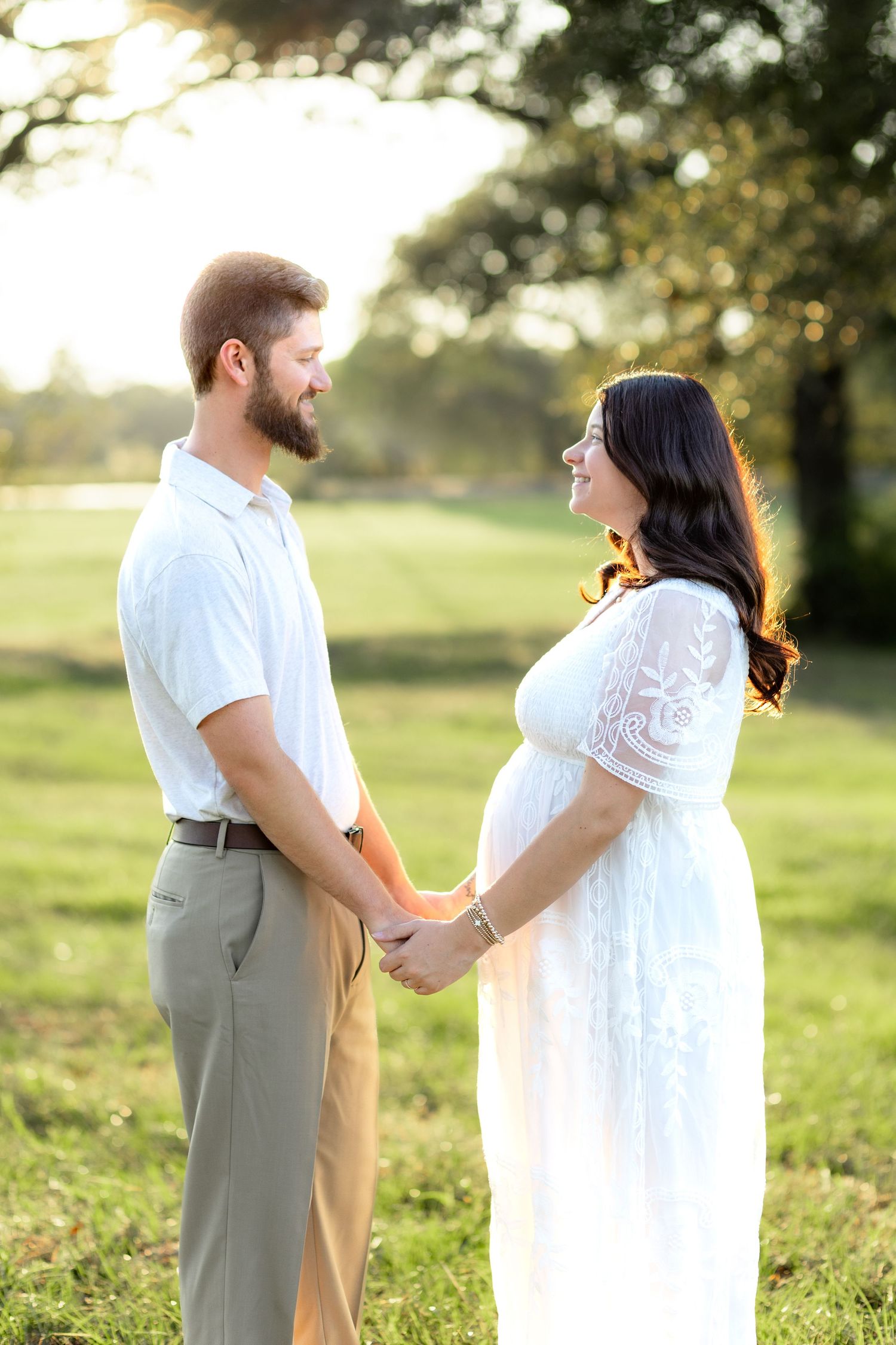 Expecting couple holding hands in a grass field at sunset in Dothan, Alabama