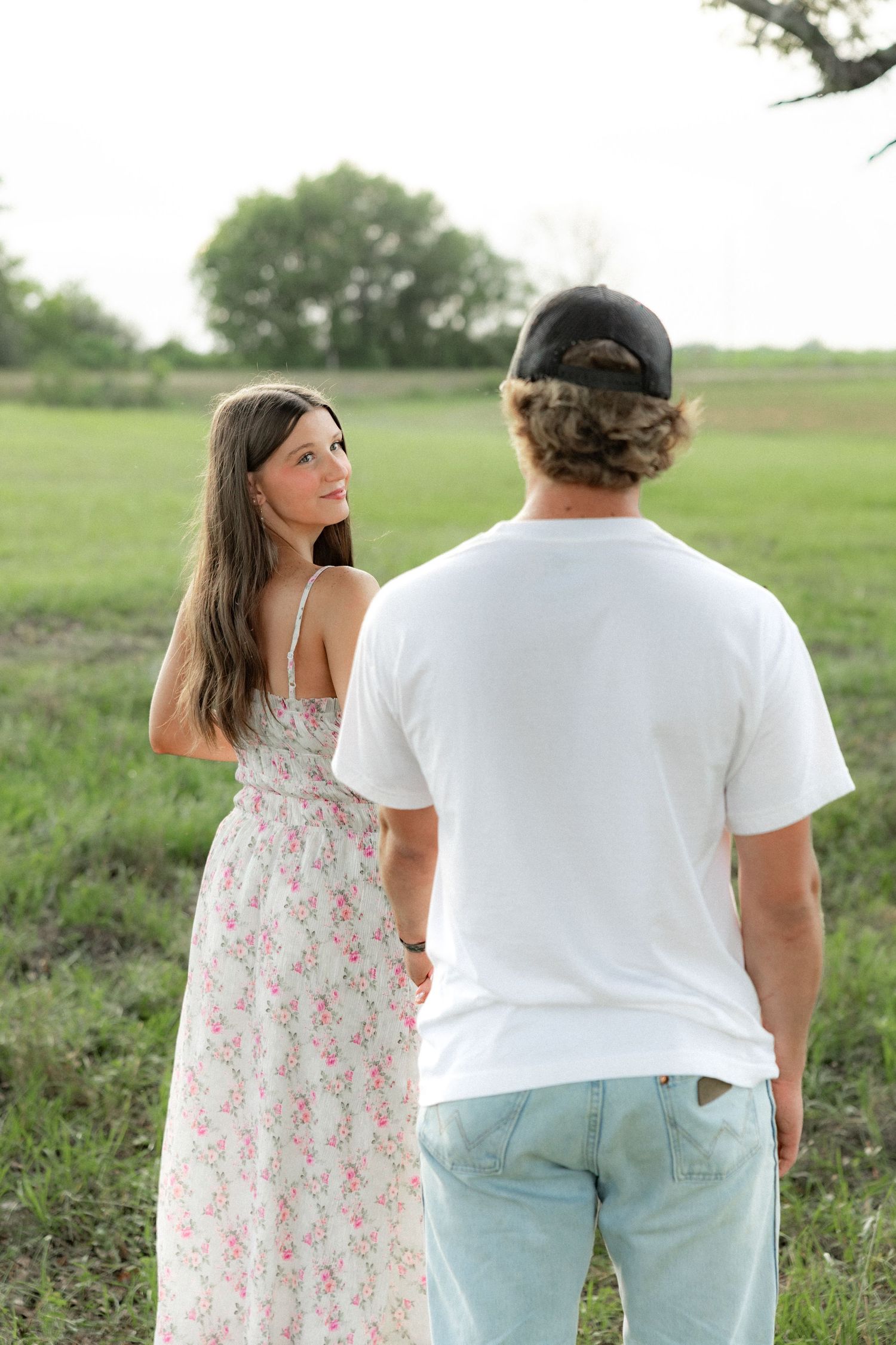 Romantic couple photos in a natural grass field setting with large trees at sunset.