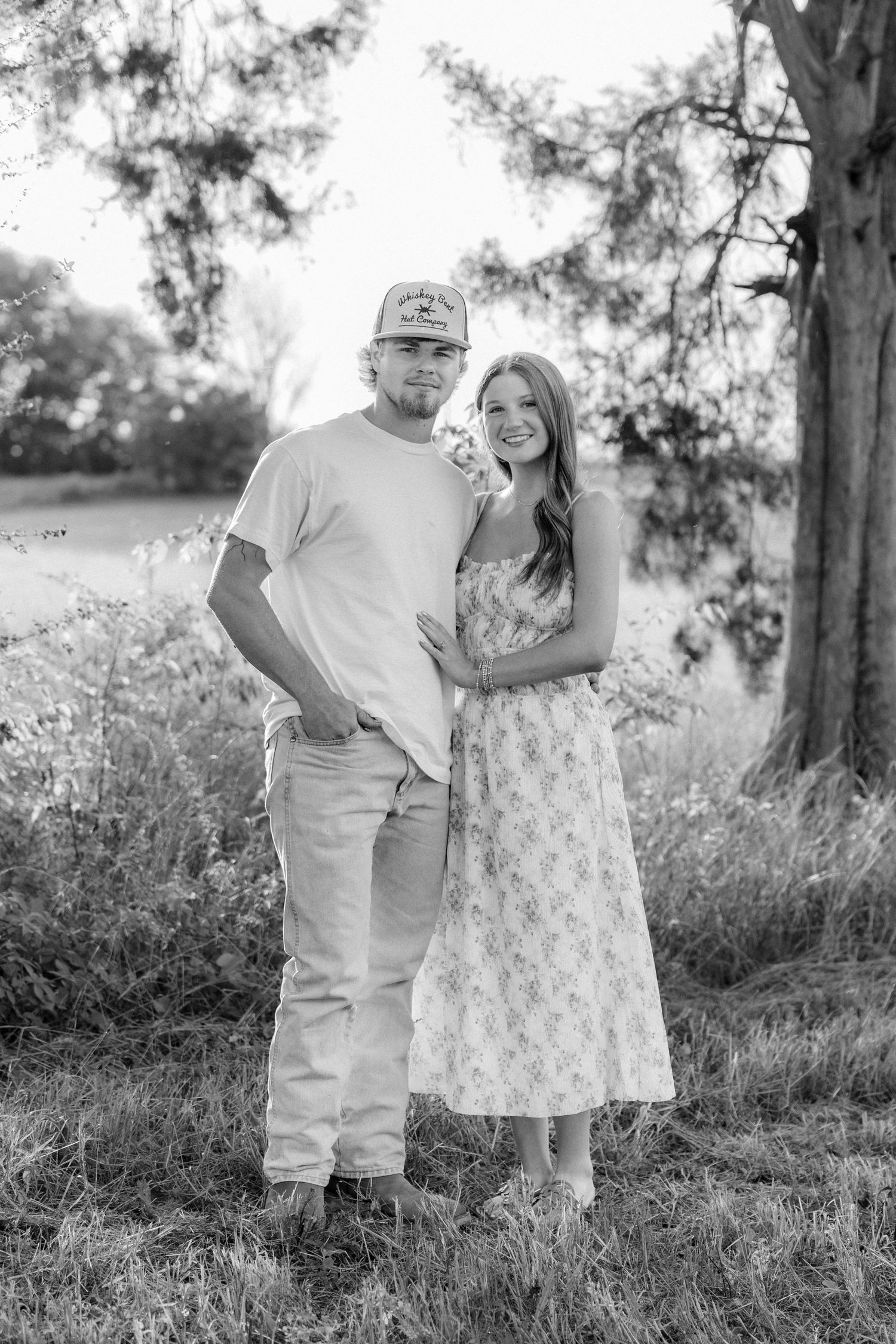 Romantic couple photos in a natural grass field setting with large trees at sunset.