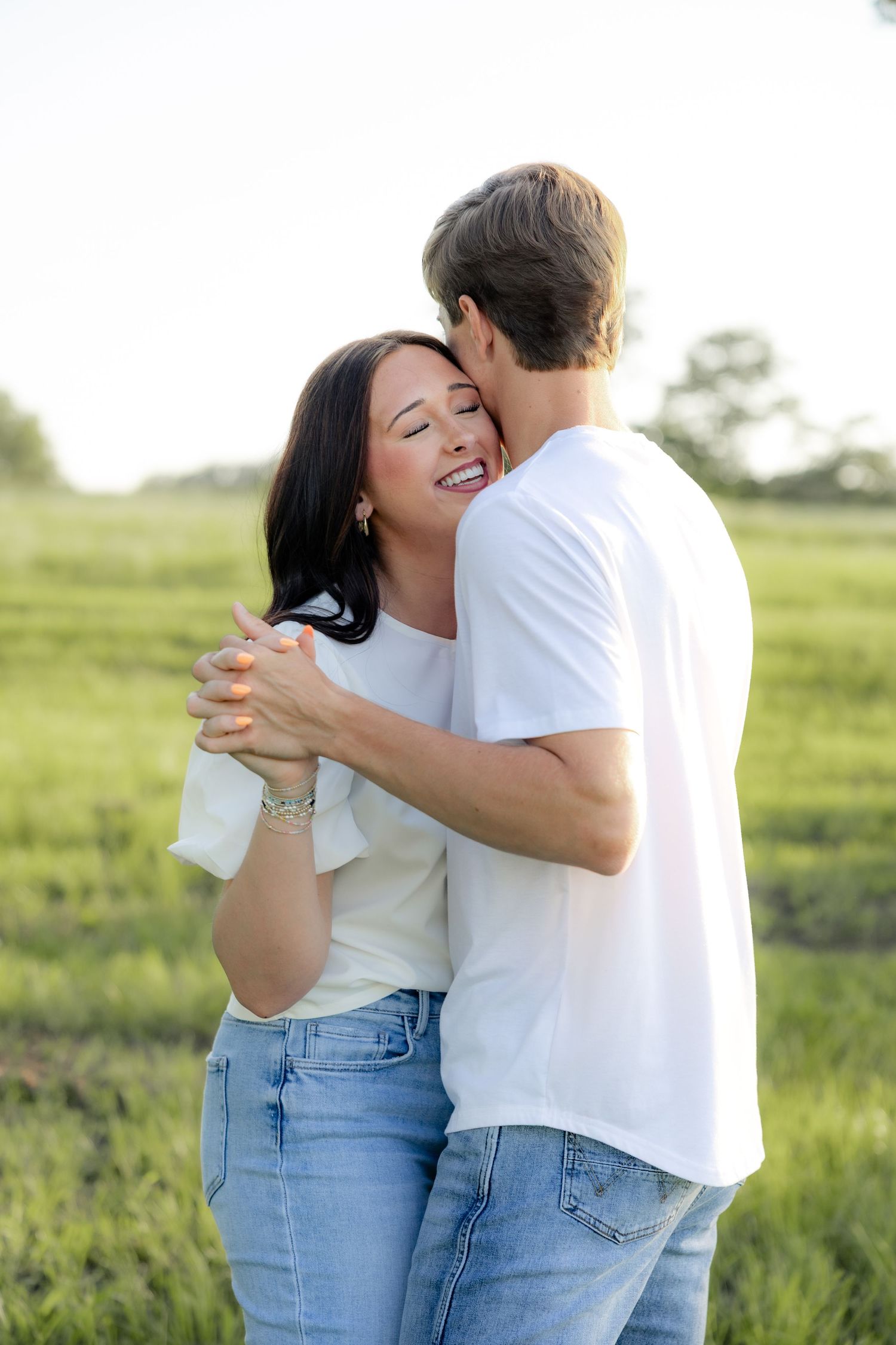 Romantic couple photos in a natural grass field setting with large trees at sunset.