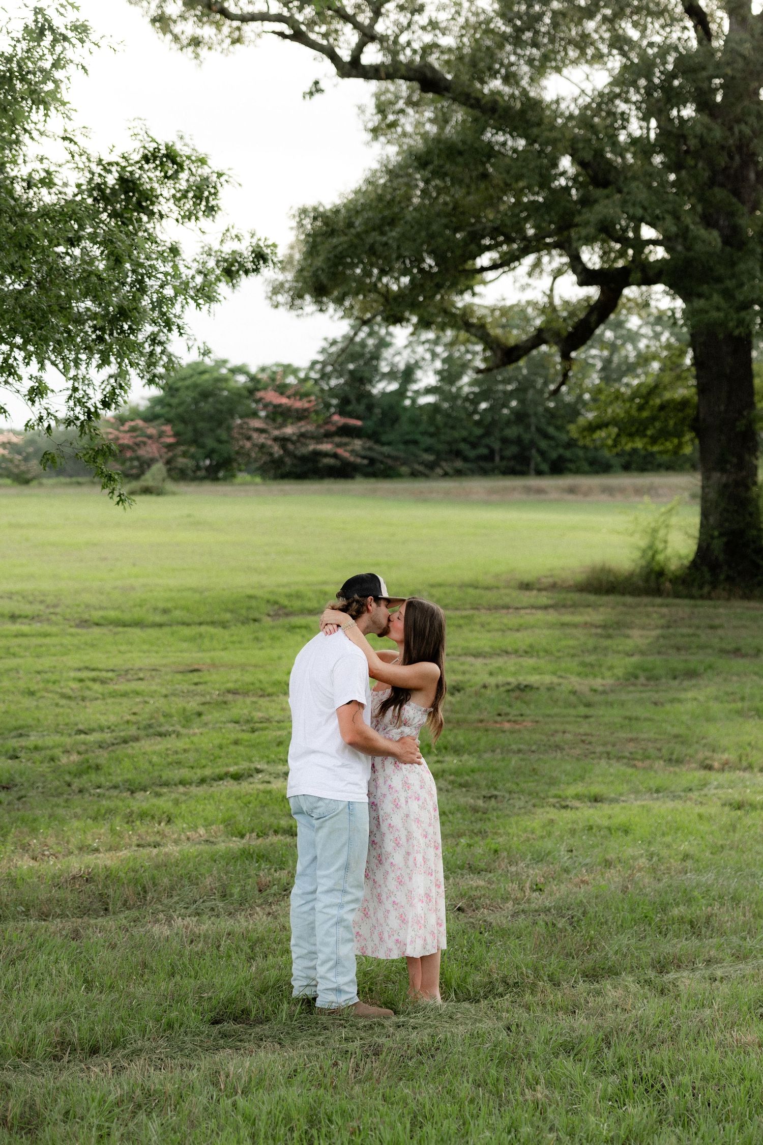 Romantic couple photos in a natural grass field setting with large trees at sunset.