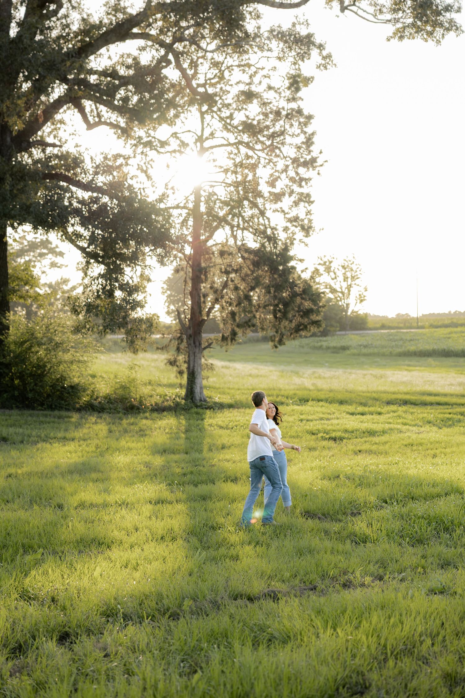 Romantic couple photos in a natural grass field setting with large trees at sunset.