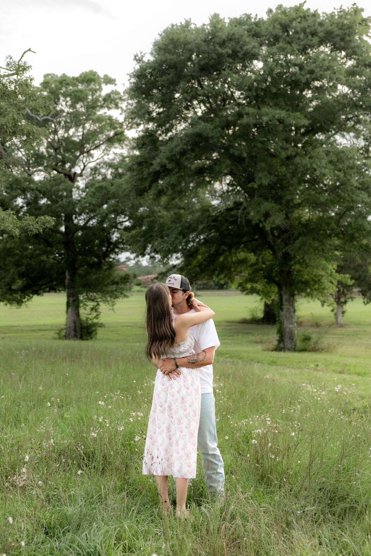 Romantic couple photos in a natural grass field setting with large trees at sunset.