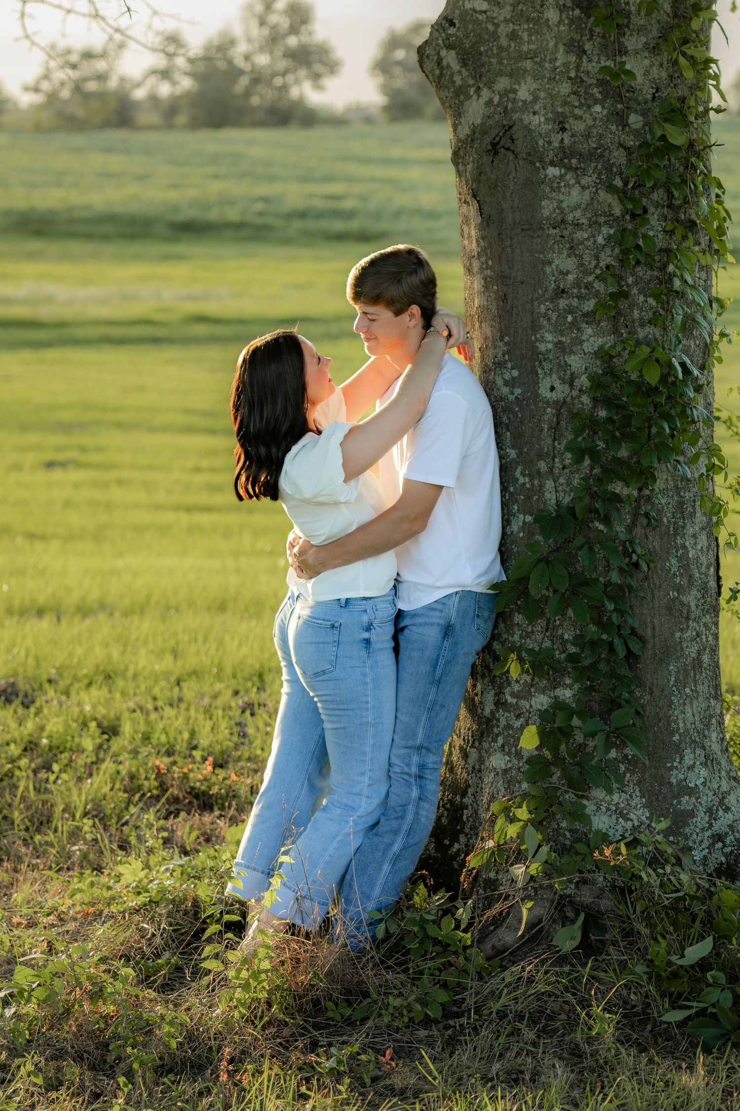 Romantic couple photos in a natural grass field setting with large trees at sunset.