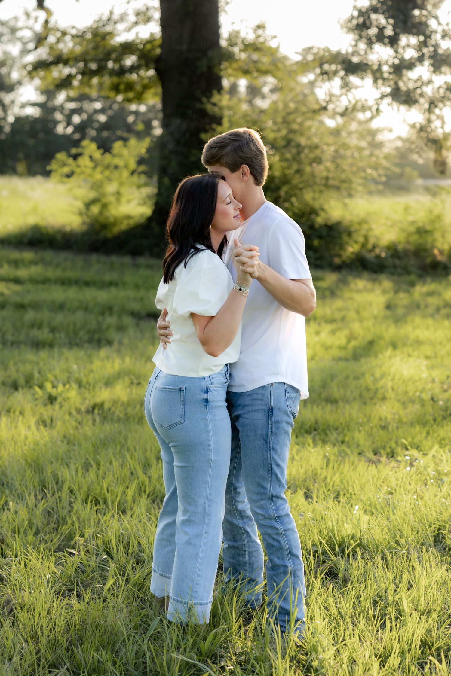 Romantic couple photos in a natural grass field setting with large trees at sunset.
