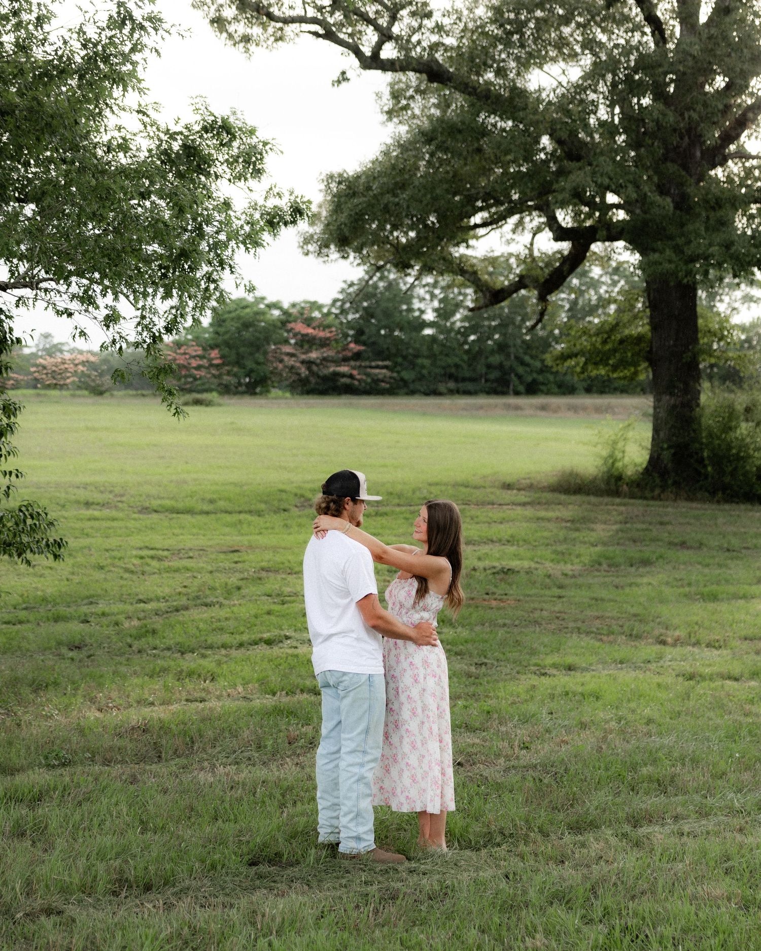 Romantic couple photos in a natural grass field setting with large trees at sunset.