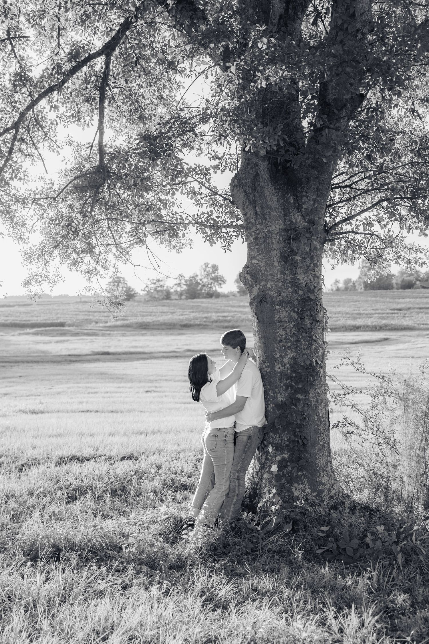 Romantic couple photos in a natural grass field setting with large trees at sunset.