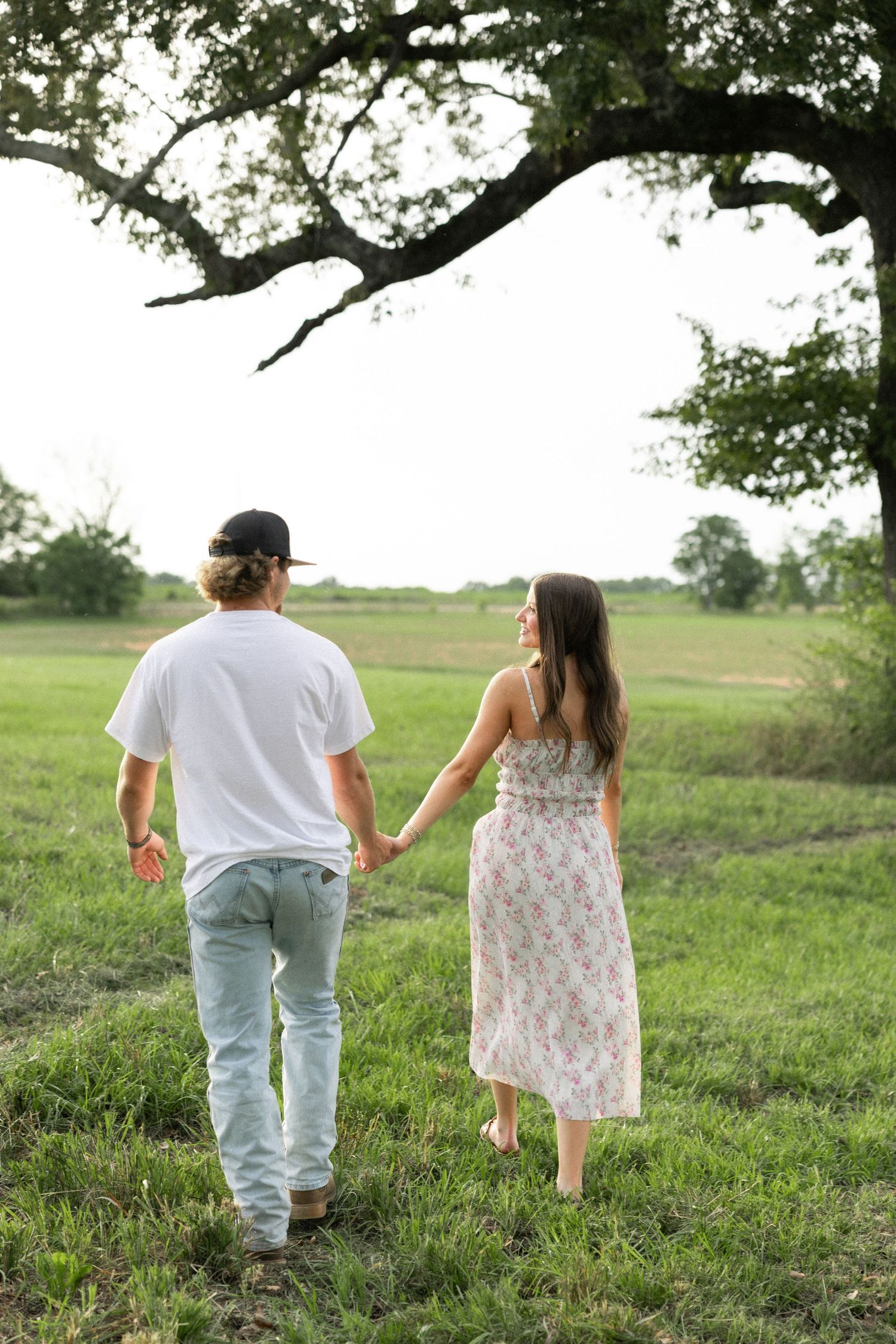 Romantic couple photos in a natural grass field setting with large trees at sunset.