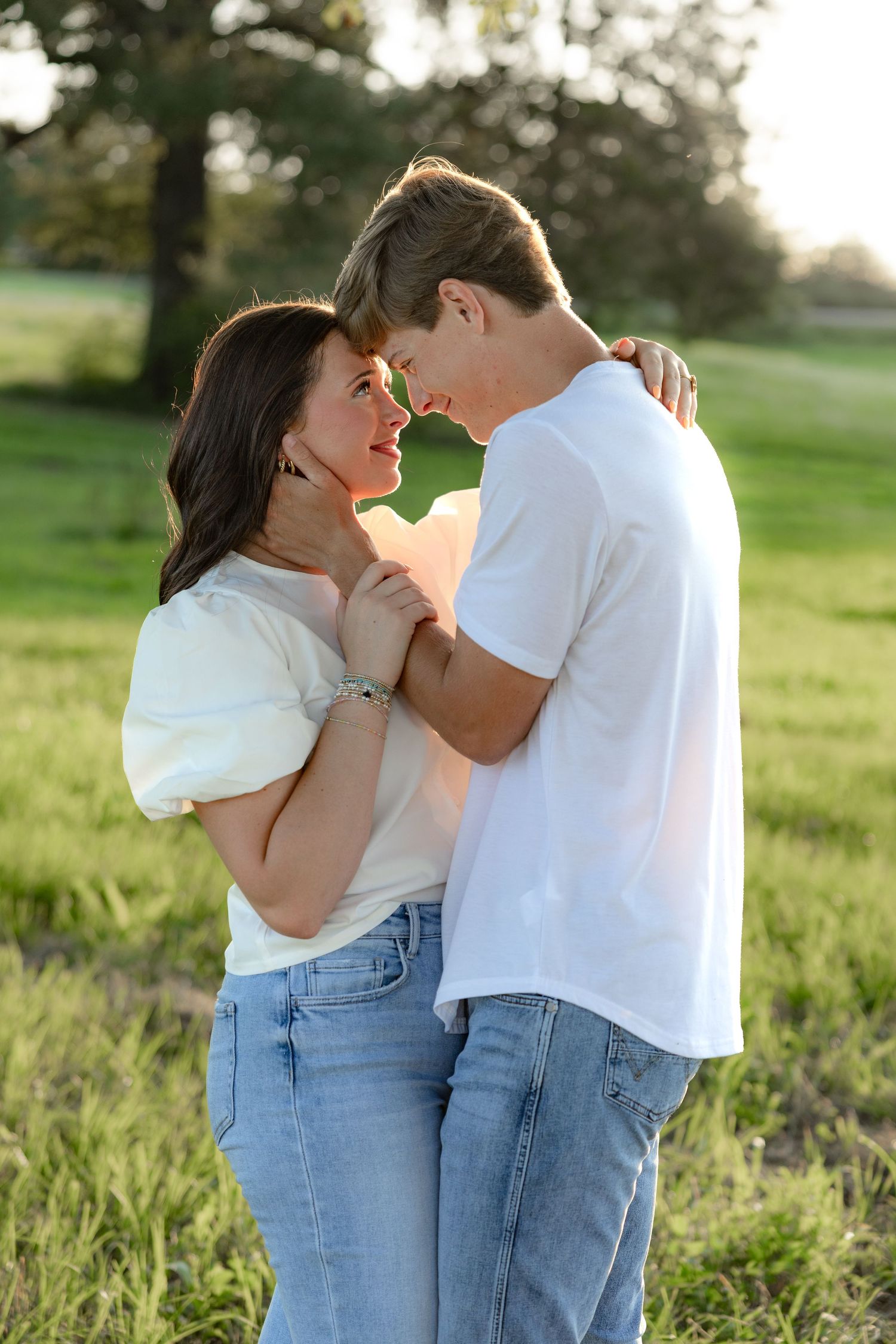 Romantic couple photos in a natural grass field setting with large trees at sunset.