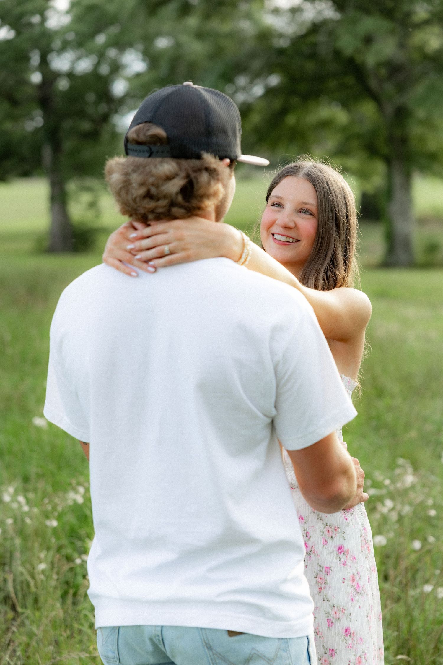Romantic couple photos in a natural grass field setting with large trees at sunset.