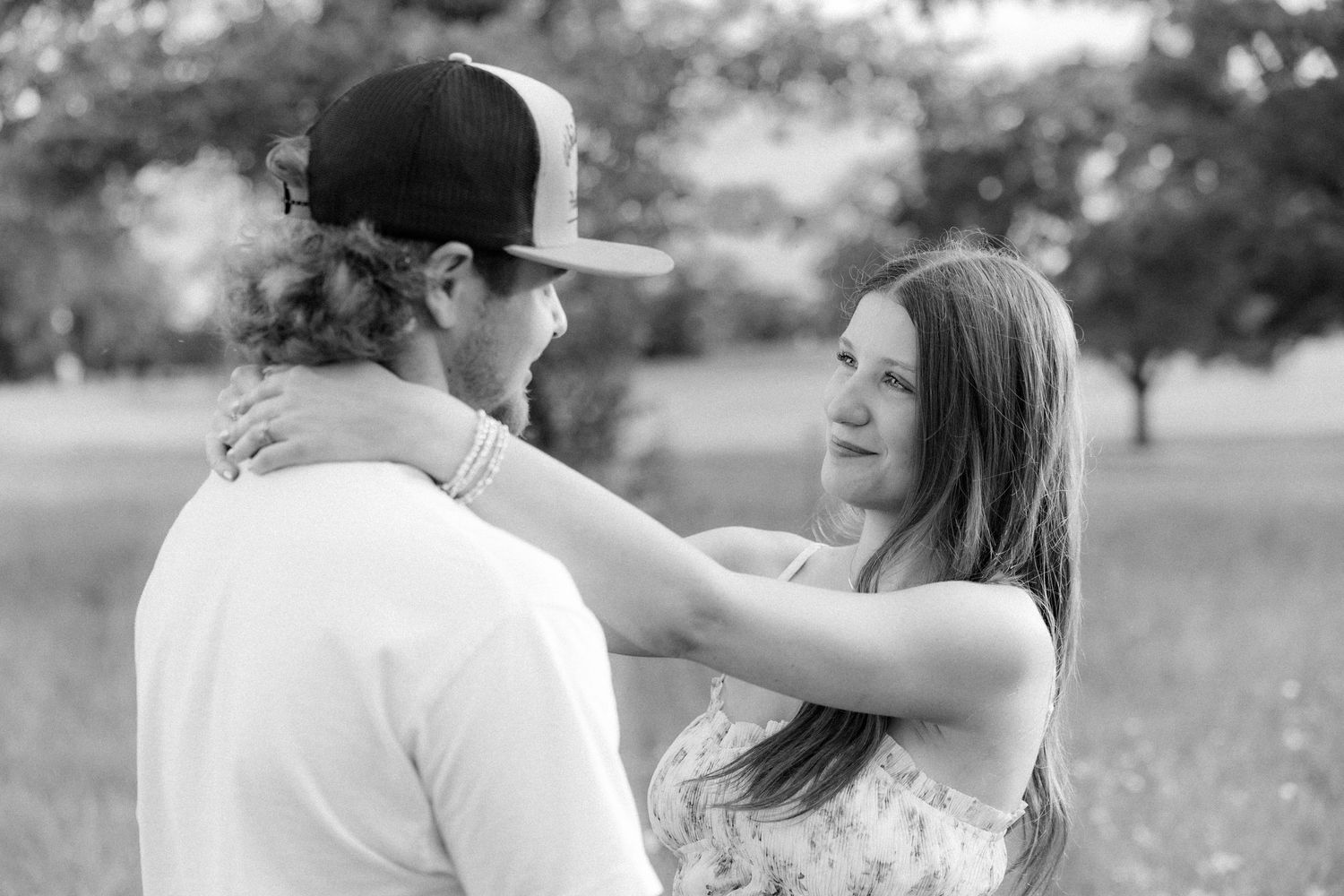 Romantic couple photos in a natural grass field setting with large trees at sunset.