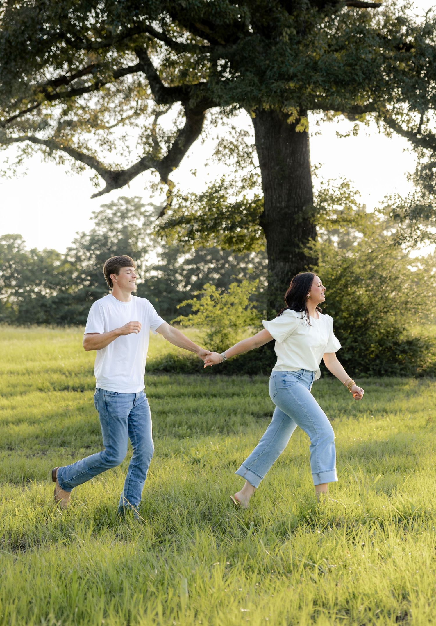 Romantic couple photos in a natural grass field setting with large trees at sunset.