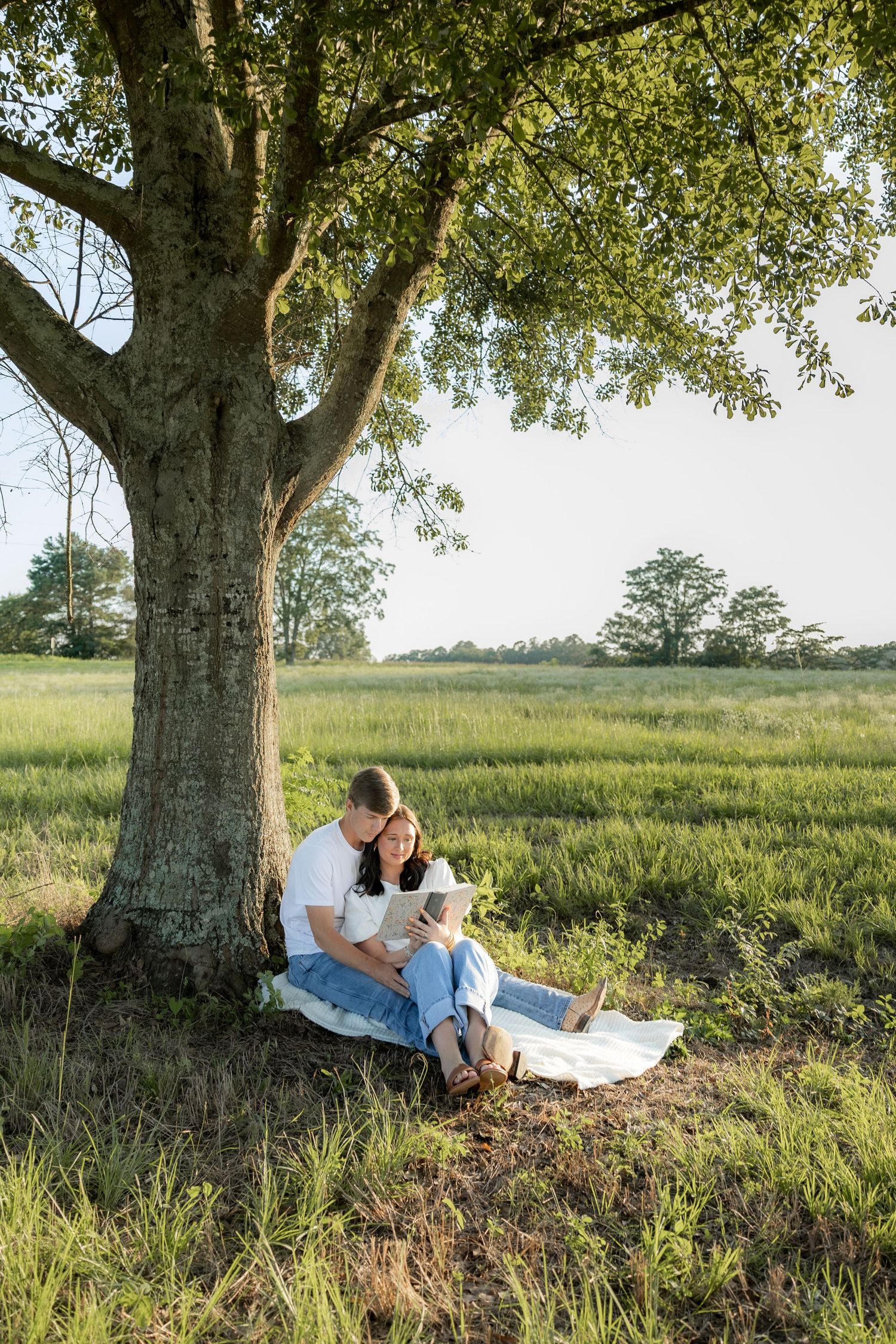 Romantic couple photos in a natural grass field setting with large trees at sunset.