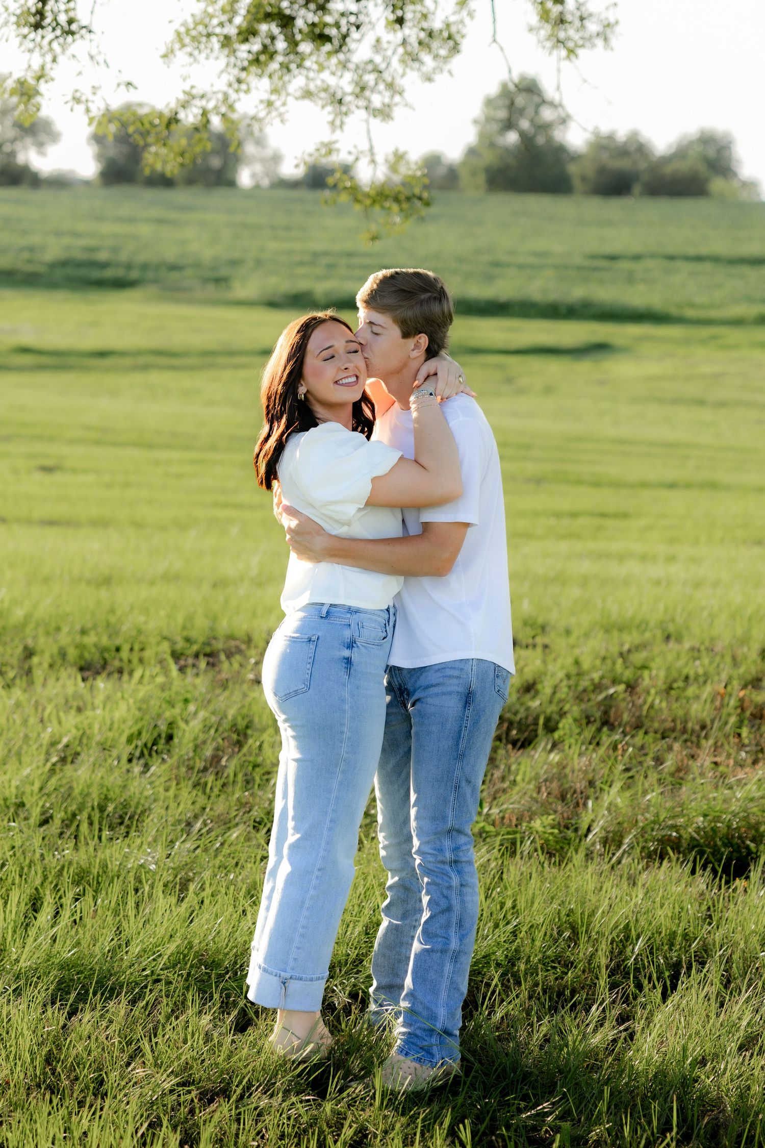Romantic couple photos in a natural grass field setting with large trees at sunset.