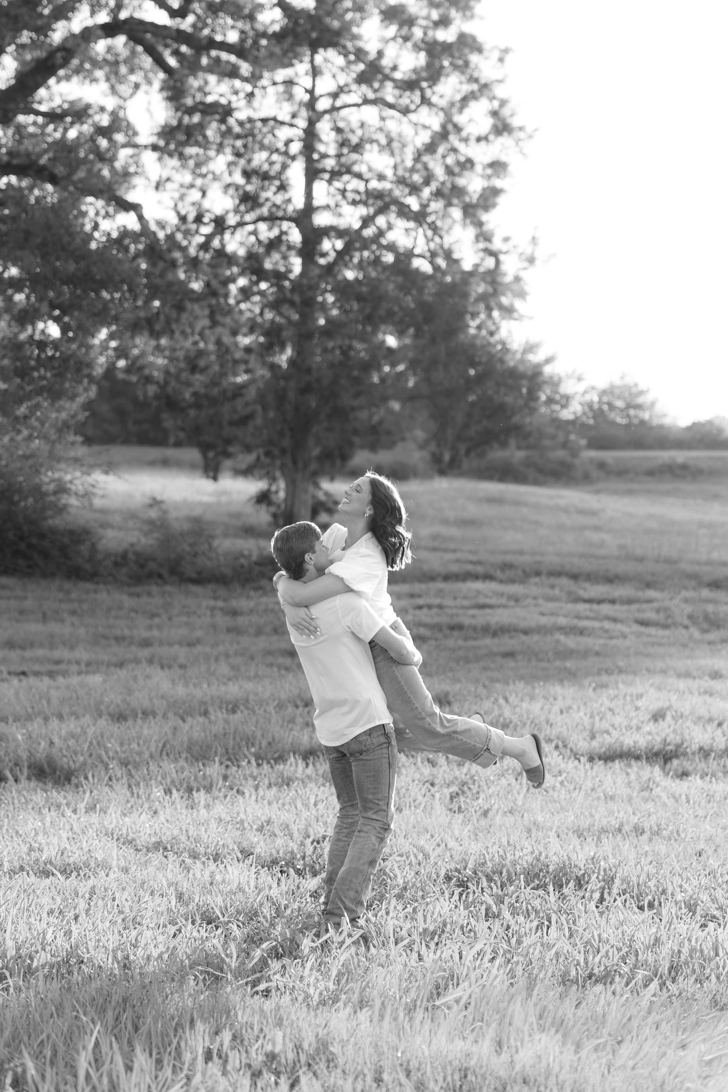 Romantic couple photos in a natural grass field setting with large trees at sunset.
