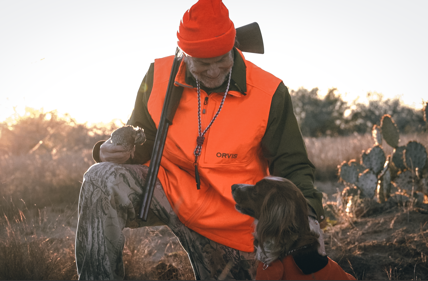 Hunter wearing orange safety vest and red beanie checking gear in morning light.