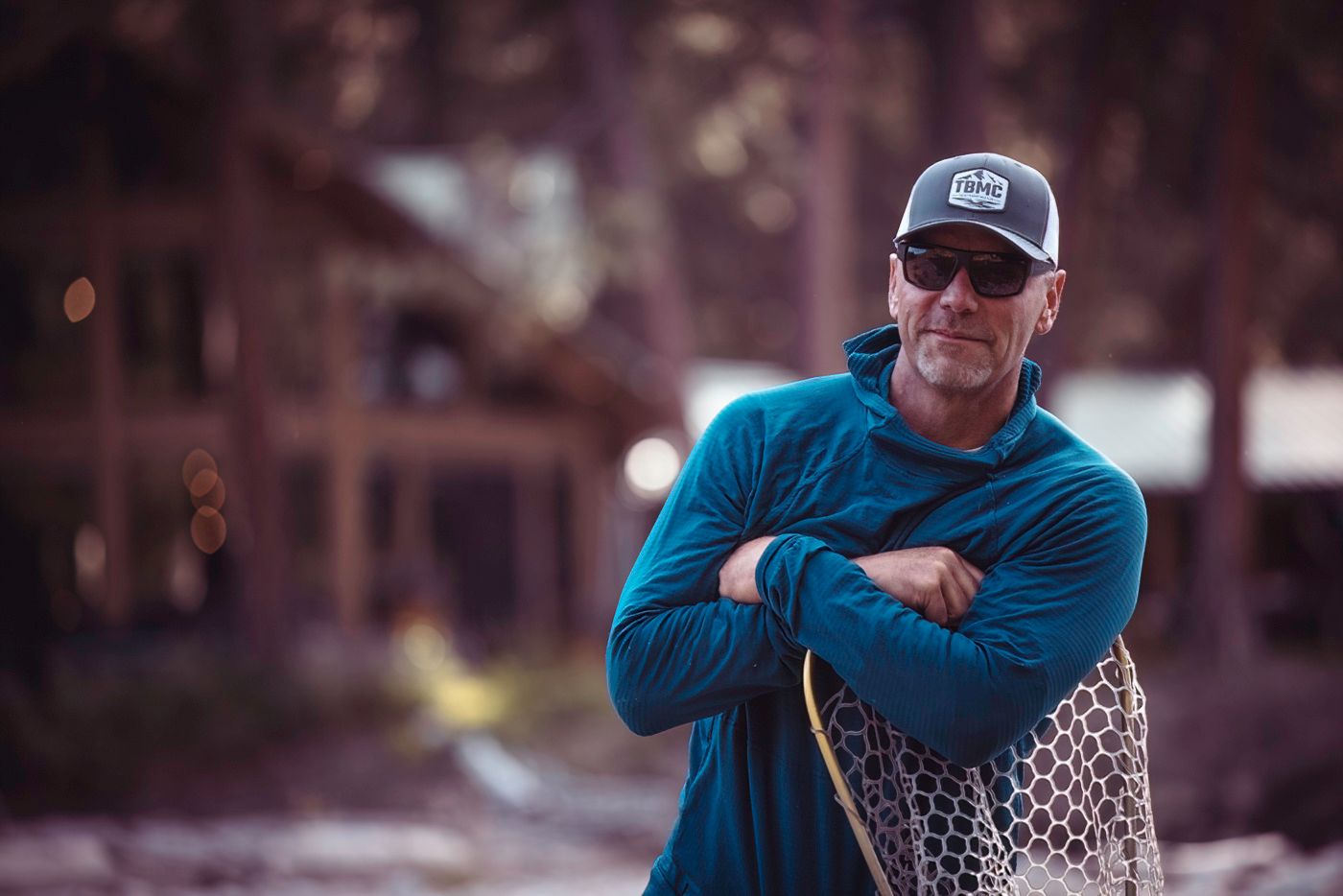 Fly fisherman in blue shirt holding fishing net by the river.
