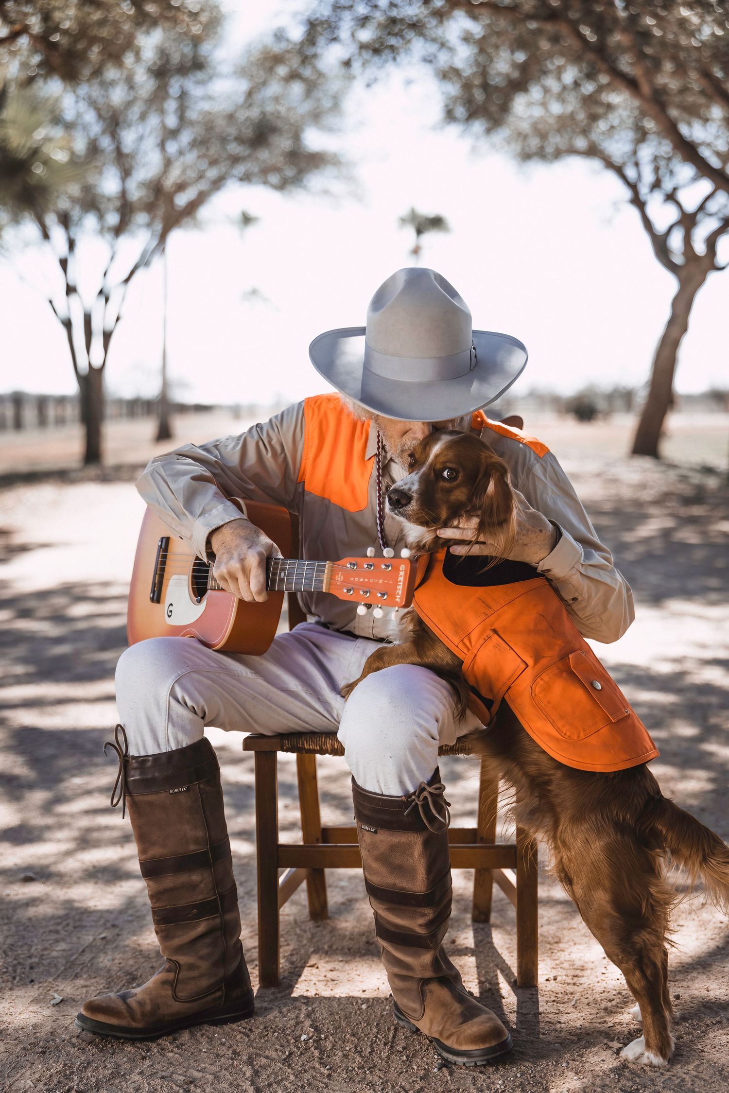A cowboy plays acoustic guitar while a friendly dog shows affection.