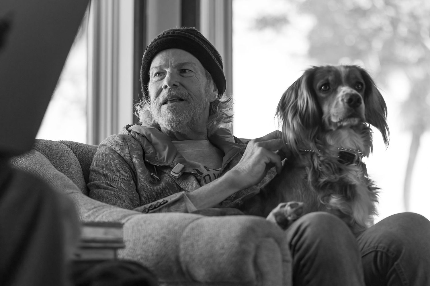 Indoor scene with person and dog relaxing by window in black and white.
