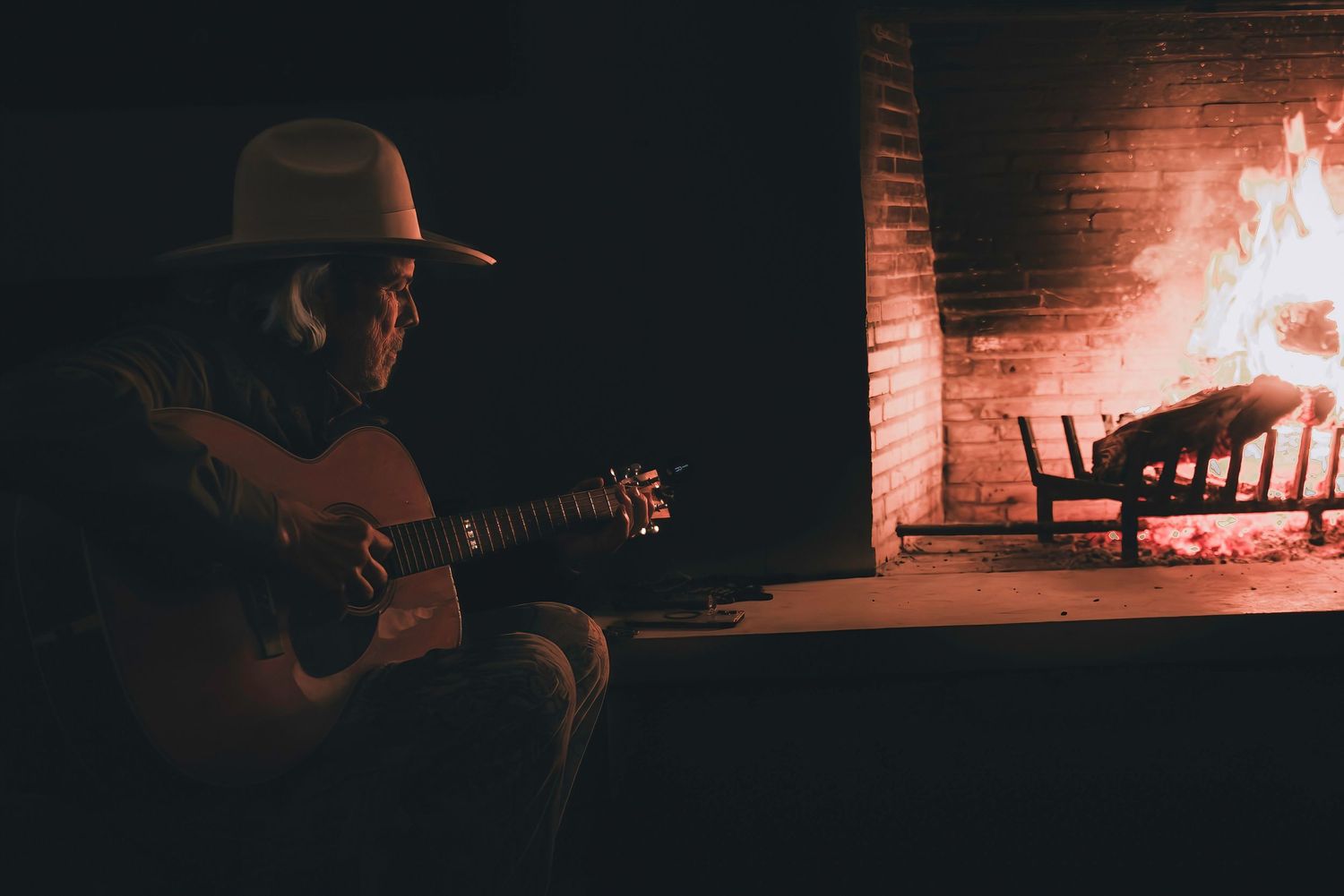 Acoustic guitar performance in dark room with glowing fireplace in background.