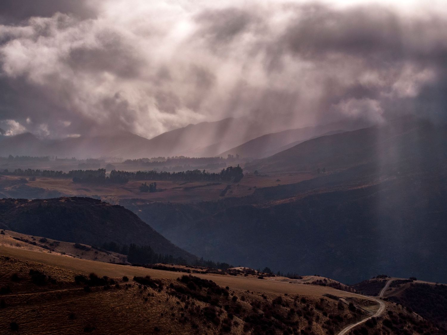 Dramatic sunbeams pierce through stormy clouds over mountainous landscape.