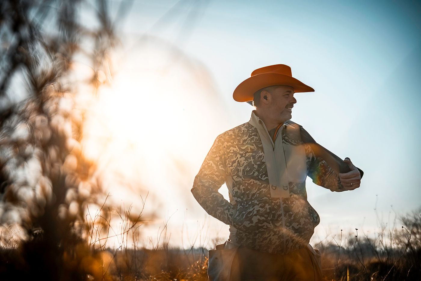 Silhouette of a hunter against golden sunset sky in a rural field.