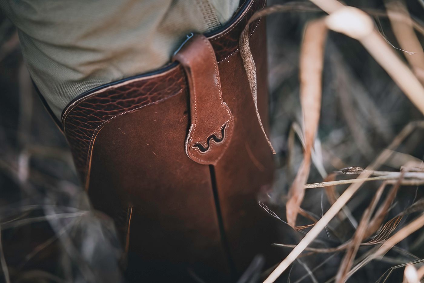 Close-up detail of worn leather hunting boots in dry grass.