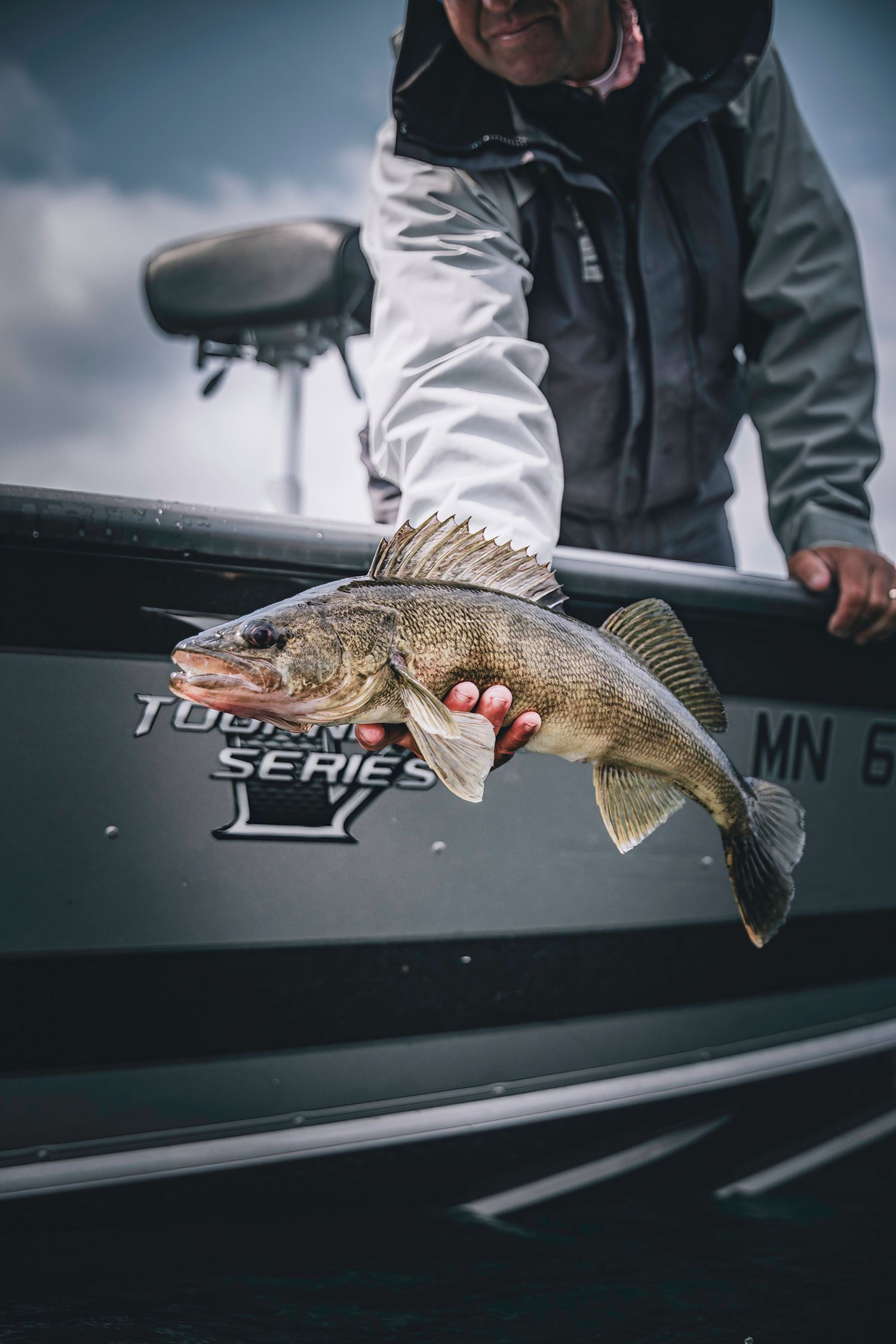 Bass fish being held alongside a fishing boat with 'Tournament Series' visible on the side.
