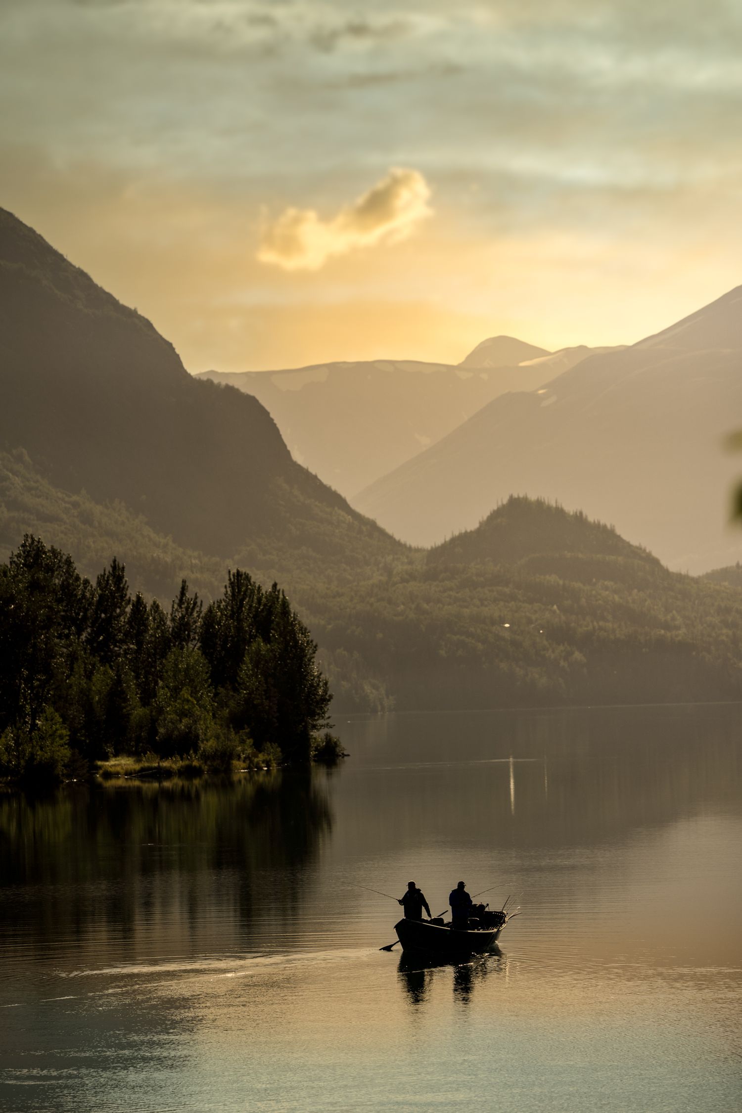 Serene lake at sunset with silhouetted mountains and a small boat in the distance.