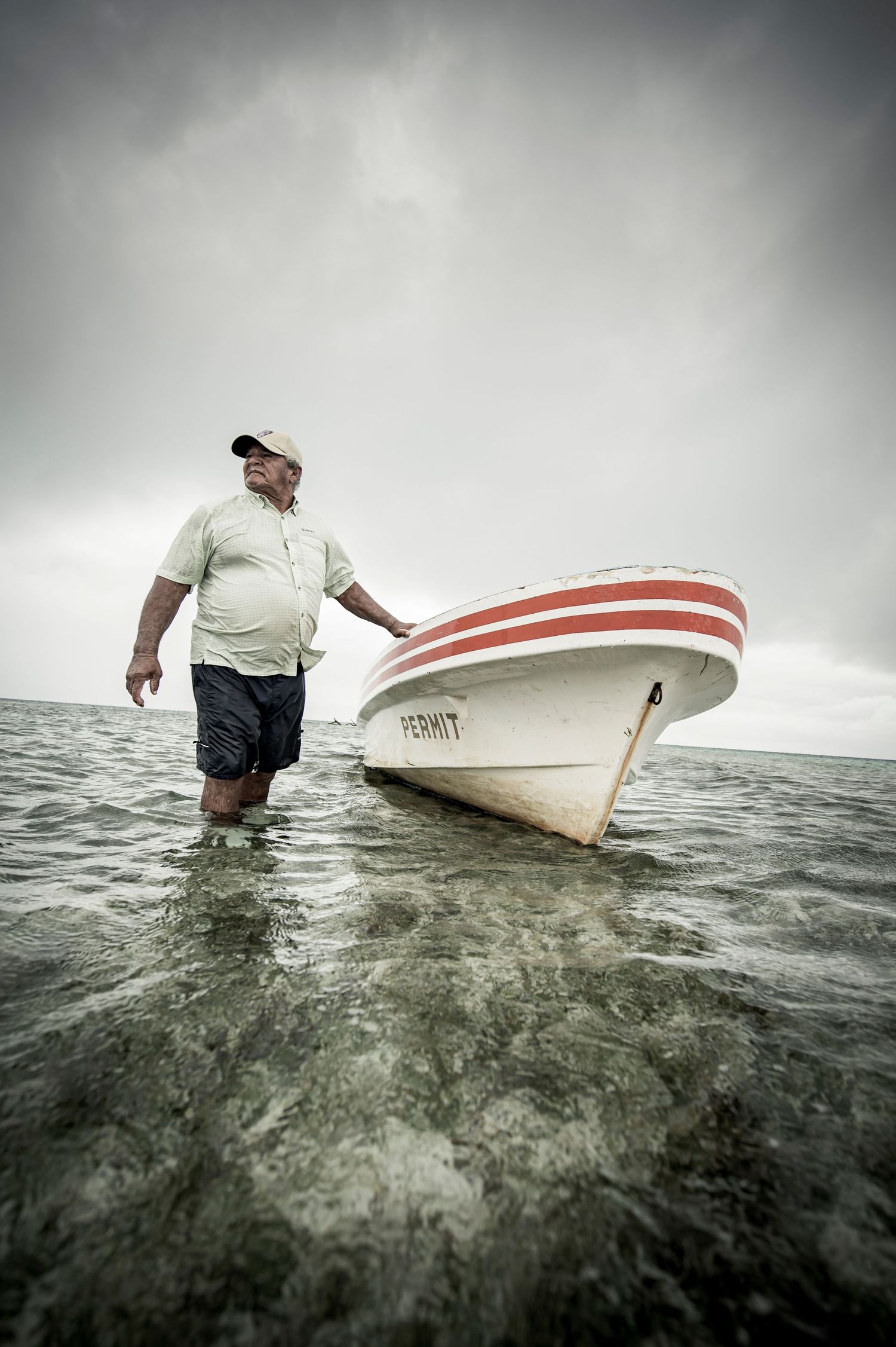 A person wades through stormy waters while pulling a small white boat in dramatic overcast conditions.