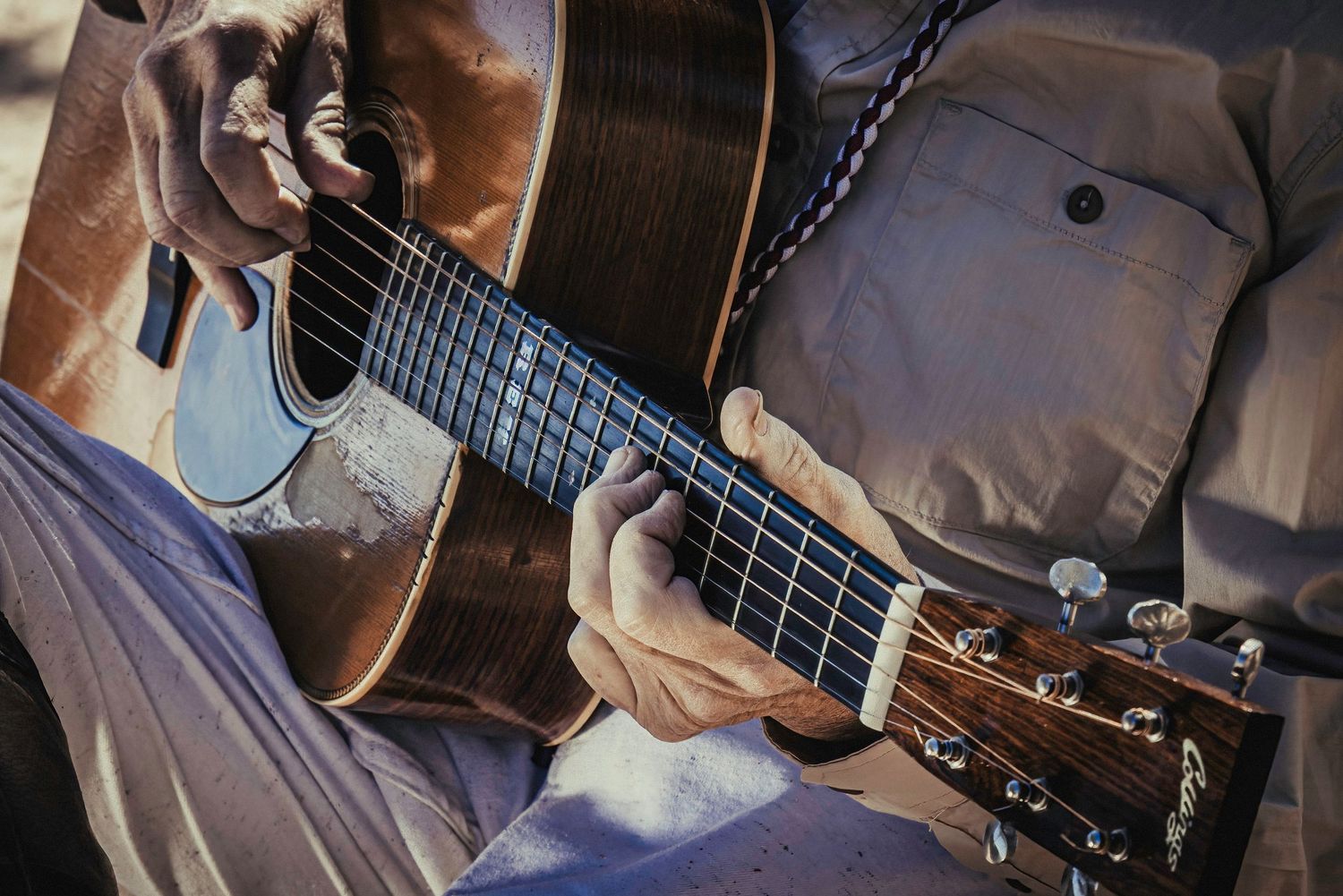 Close-up detail of hands strumming acoustic guitar strings in natural lighting.