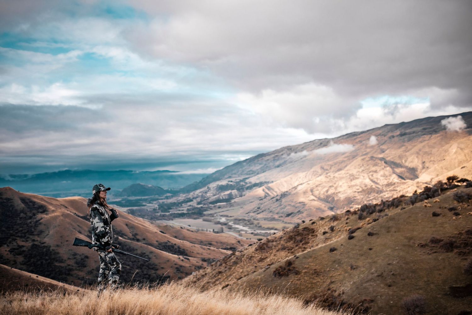 A hunter surveys the vast mountain landscape on a cloudy autumn day.