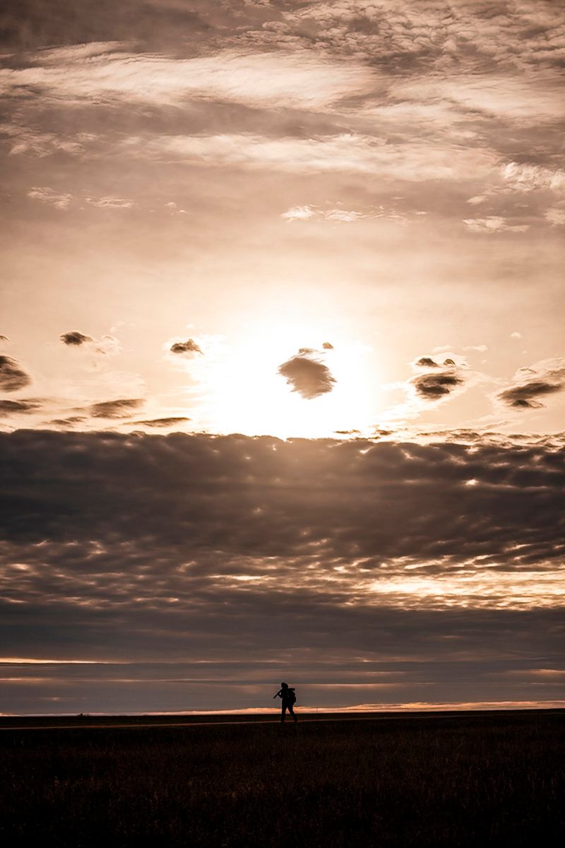 Dramatic sunset over field with small silhouette against orange sky.