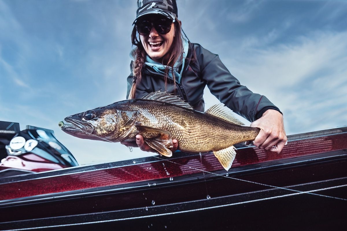 A freshly caught walleye being displayed on the edge of a red fishing boat.