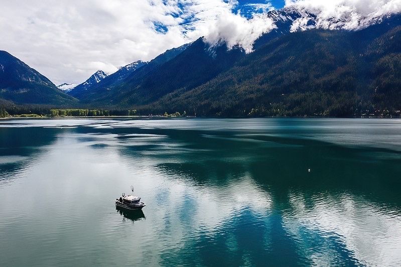 Aerial view of a small boat on turquoise mountain lake surrounded by snow-capped peaks.