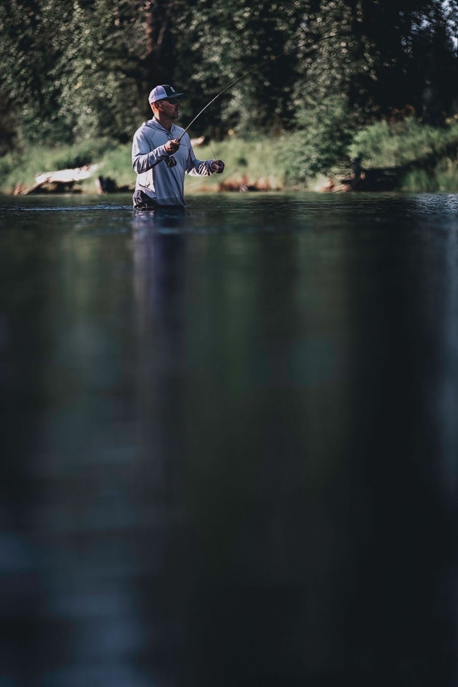 Peaceful lake scene with angler fishing from shore surrounded by pine trees.