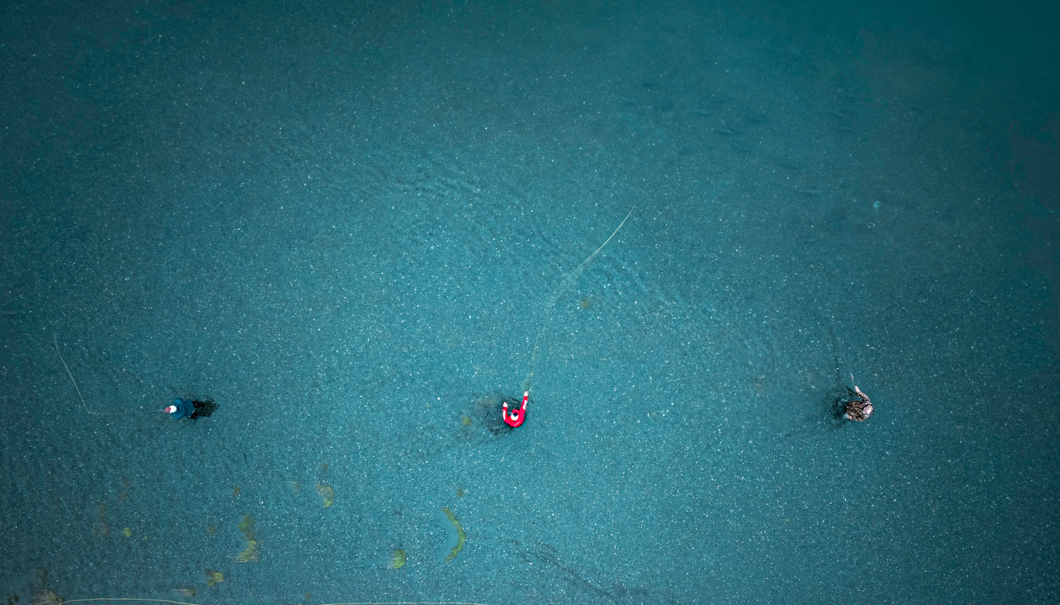 Aerial drone view of three fisherman floating in turquoise blue water from above.