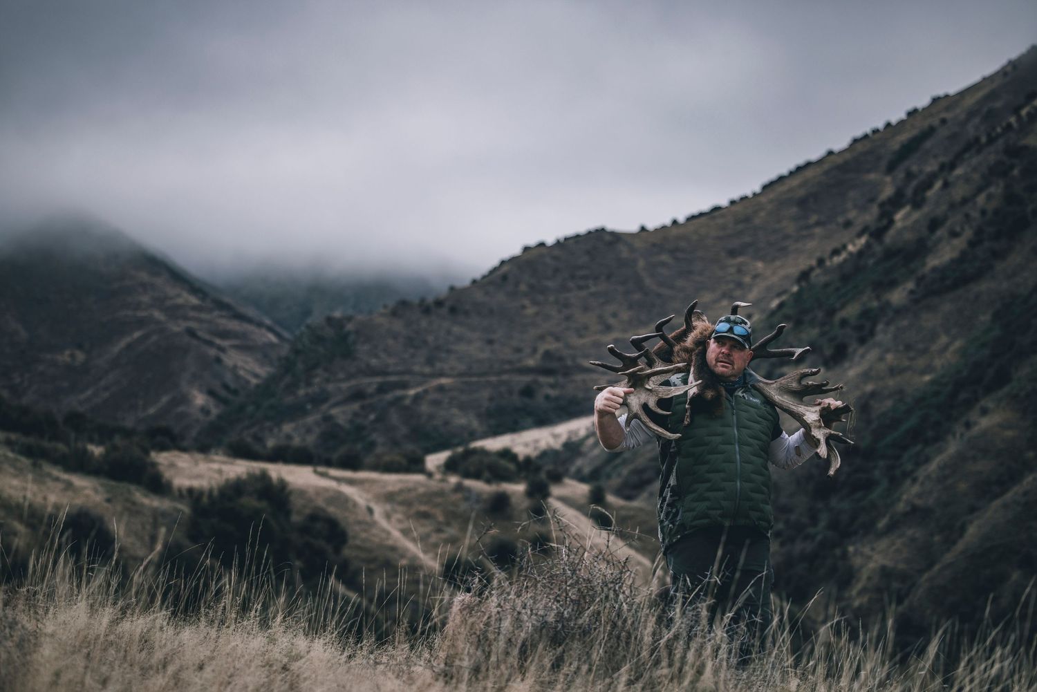 A hunter traverses a steep mountain slope with gear during an outdoor expedition.