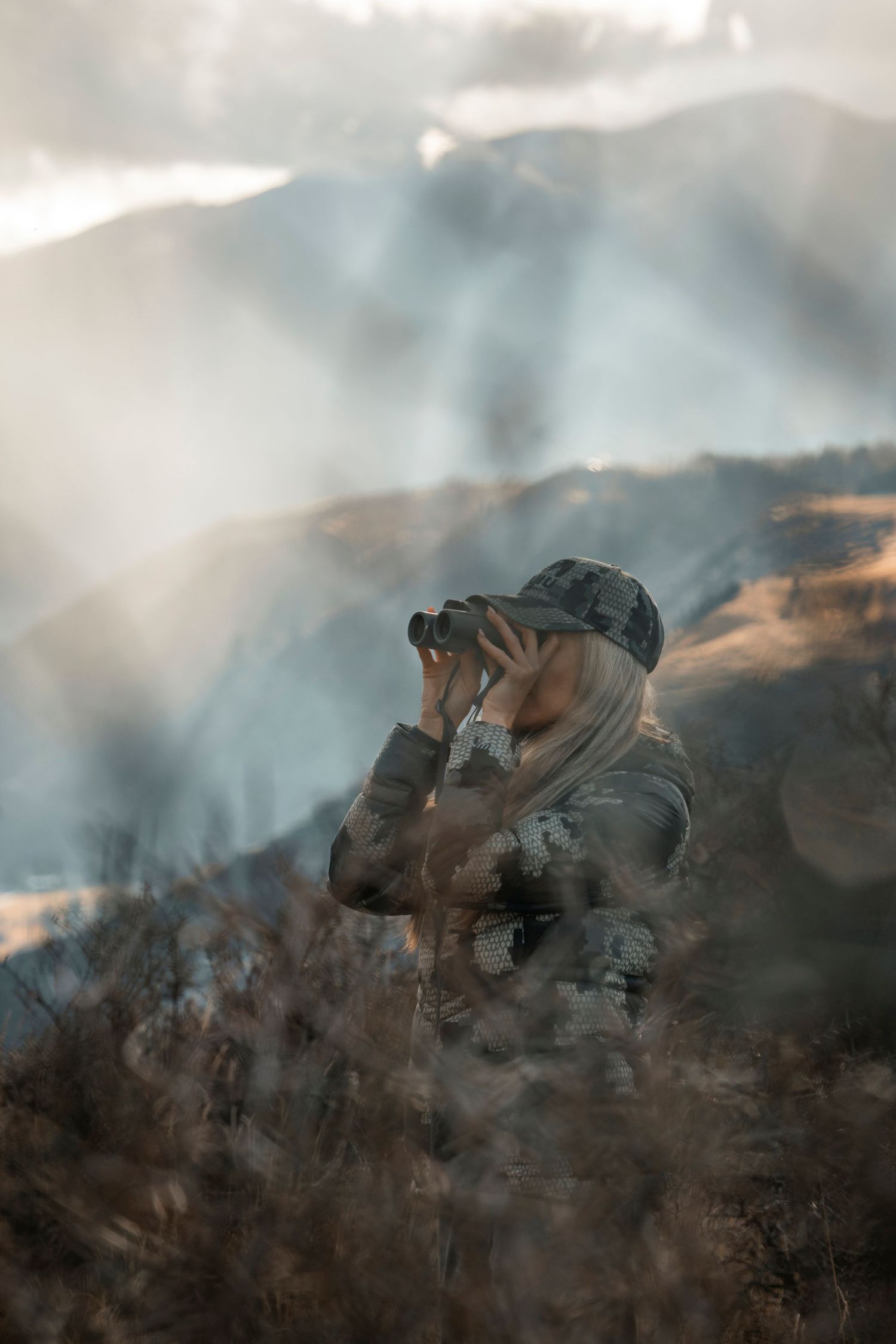 Wildlife observer using binoculars in misty mountain landscape.