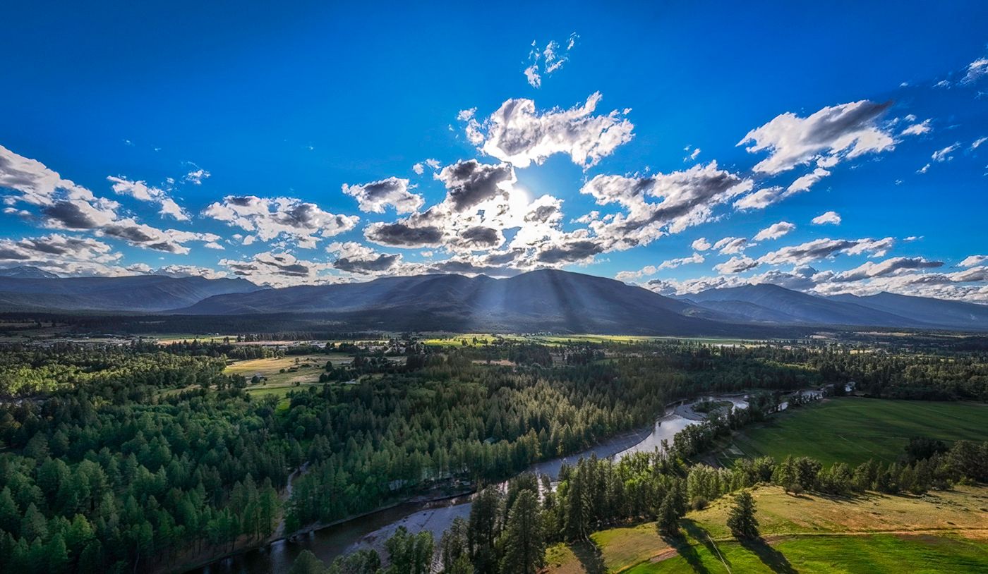 Dramatic mountain valley landscape under bright blue sky with scattered clouds.