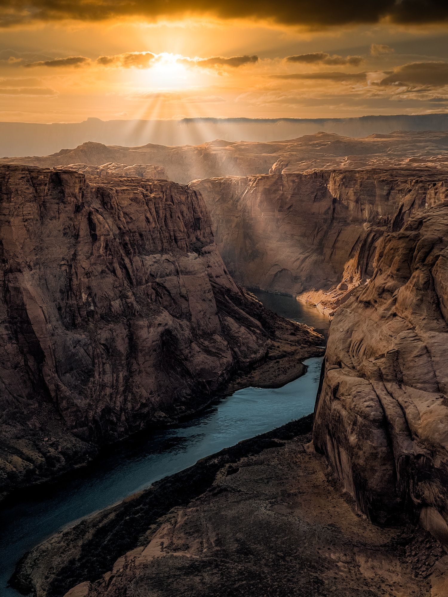 Dramatic sunset over a winding river canyon with steep cliffs and golden light.