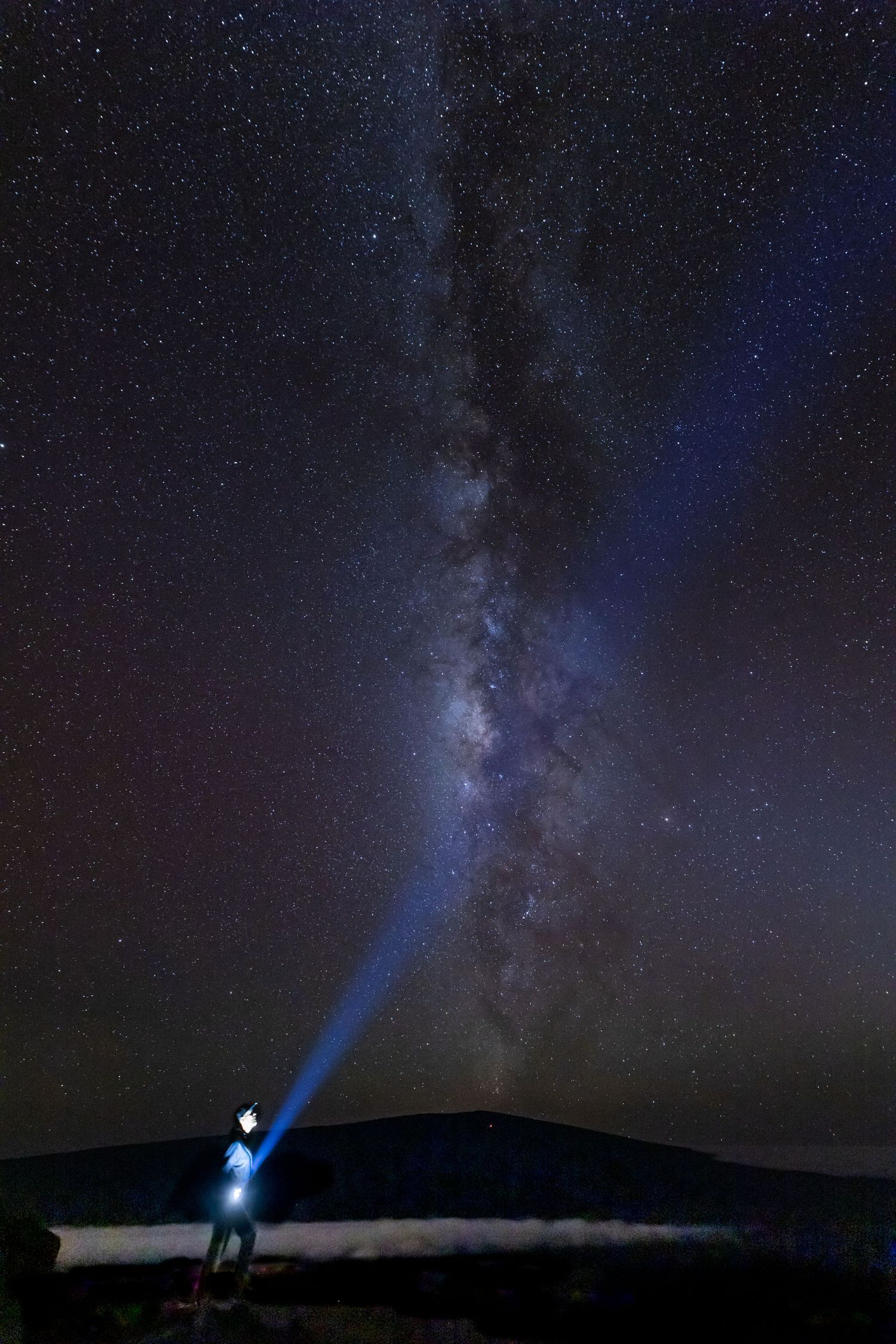 Bright flashlight beam points toward stunning Milky Way galaxy in night sky.