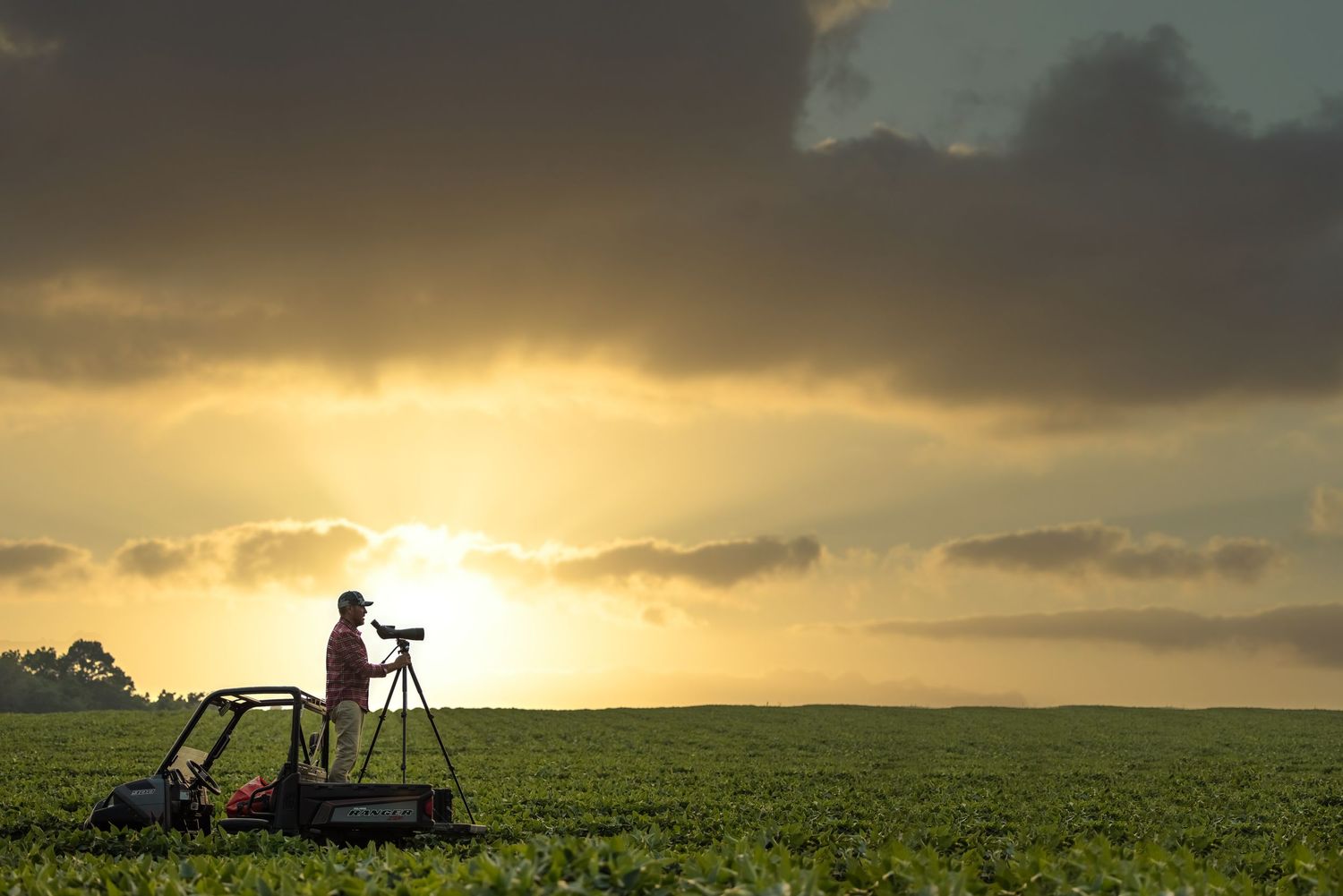 Camera equipment silhouetted against dramatic sunset sky over green field.