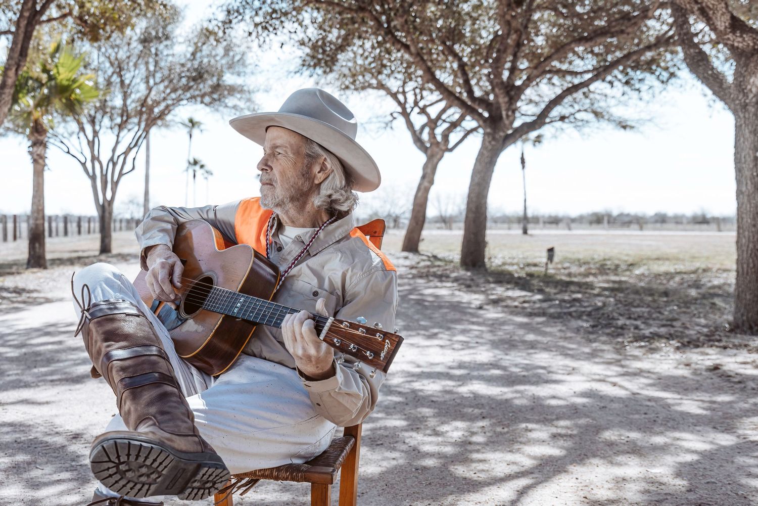 Musician with cowboy hat performing outdoors against backdrop of scattered trees.