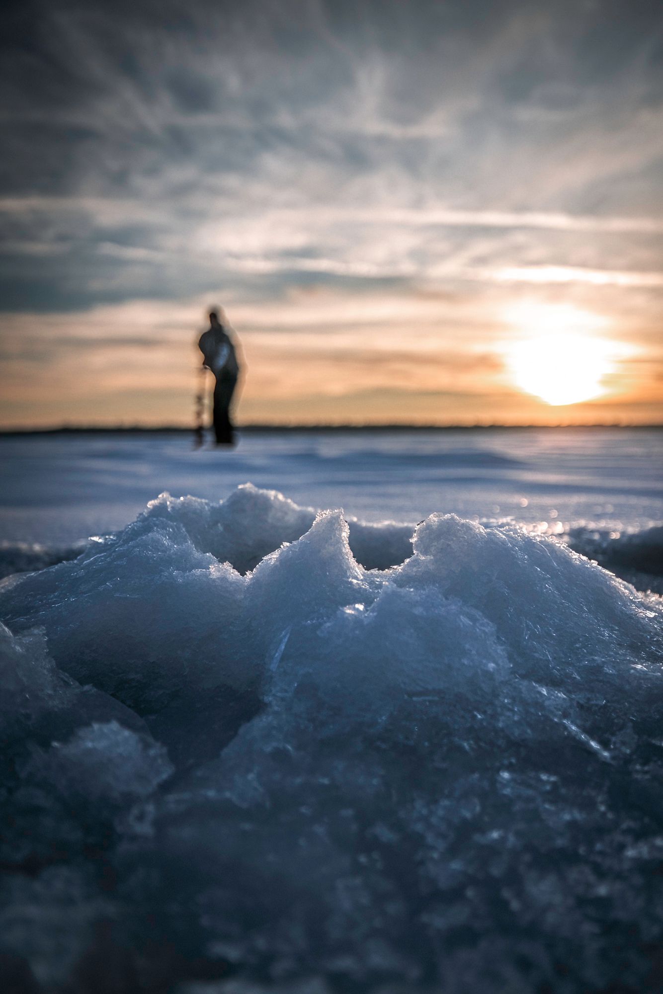 Close-up of textured ice chunks with silhouetted figure against sunset sky.