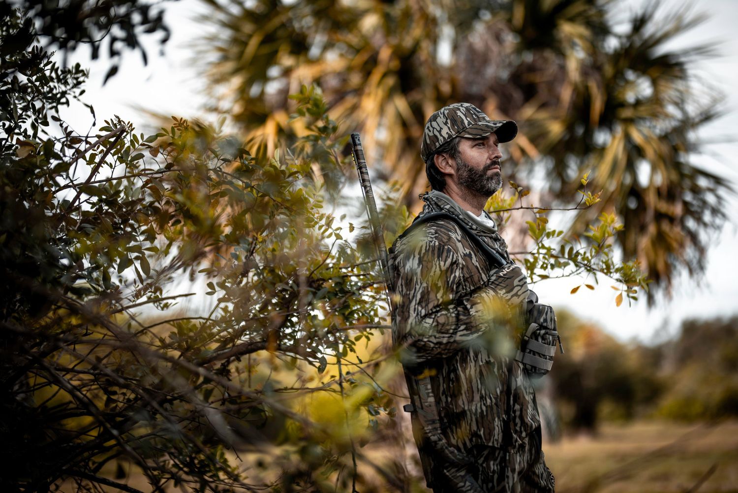 Hunter in camouflage gear standing among palm trees.