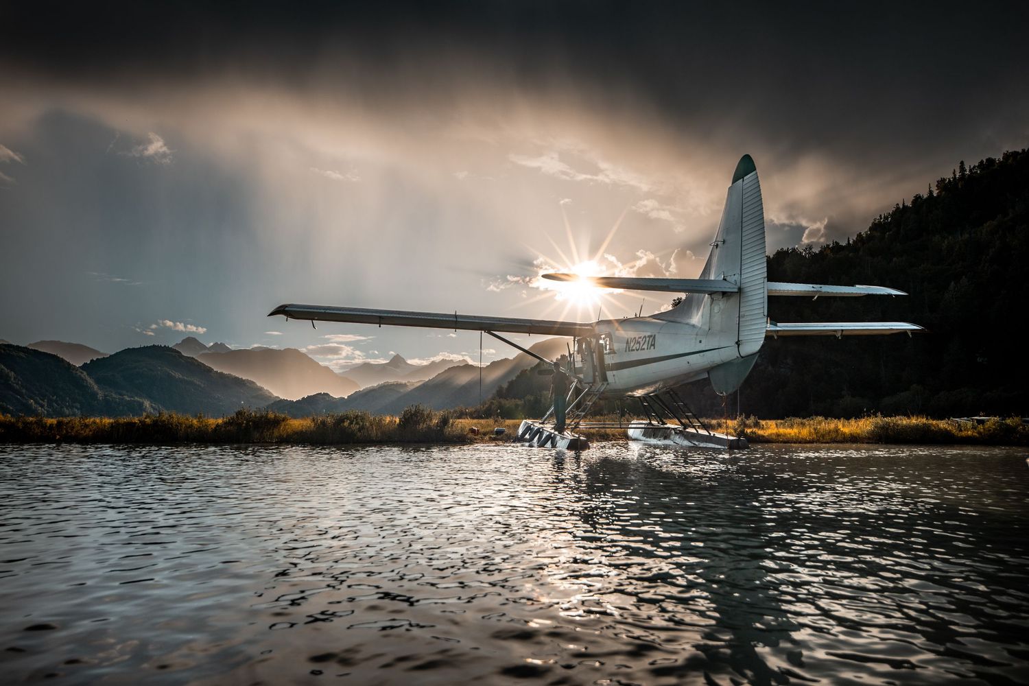 Seaplane on water with dramatic mountain landscape and moody sky.