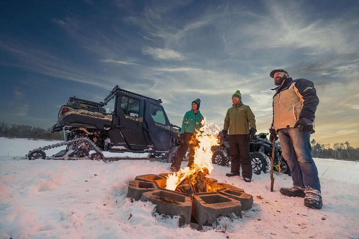 People gathered around a campfire in the snow during sunset.