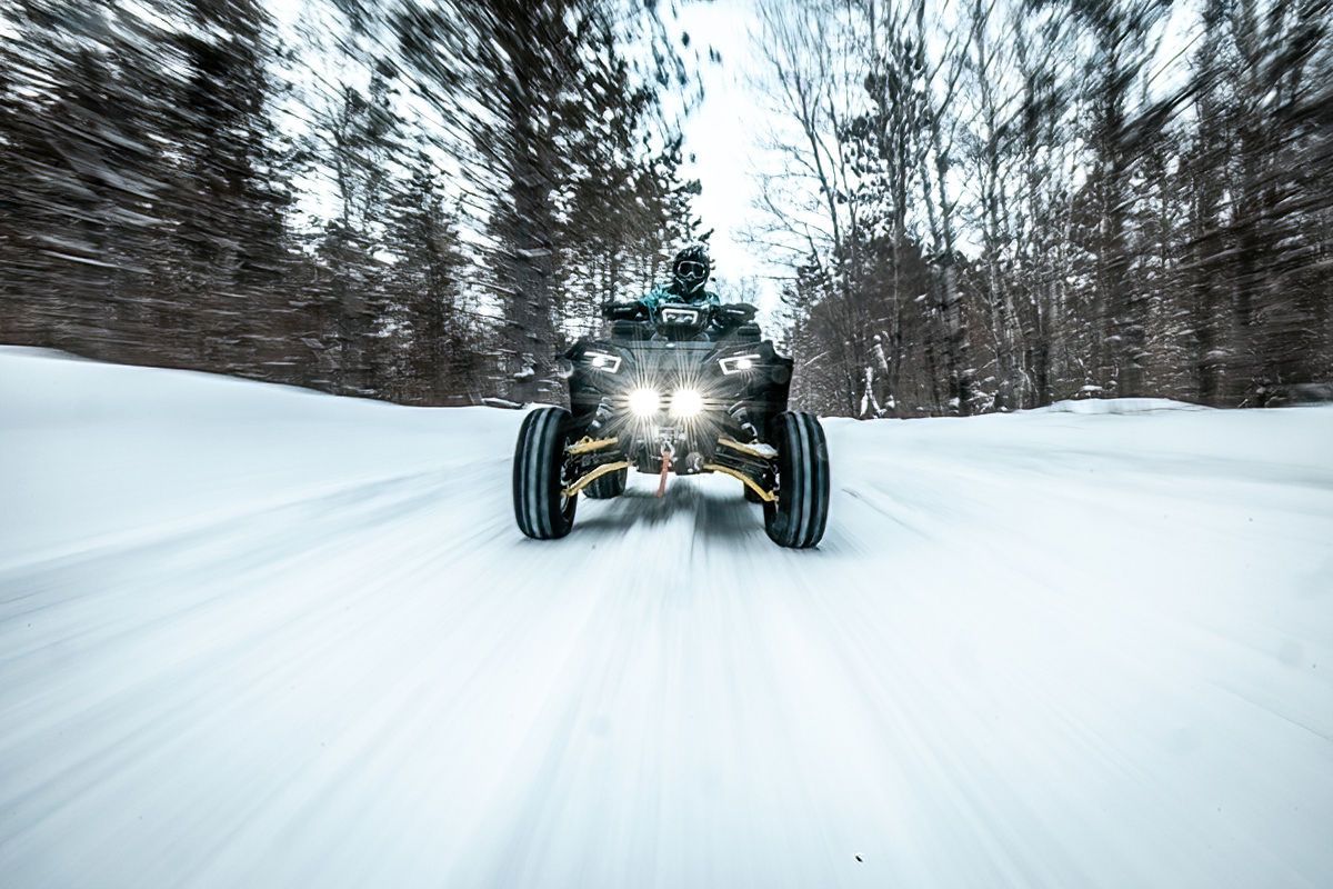ATV tracks winding through a snow-covered forest path.