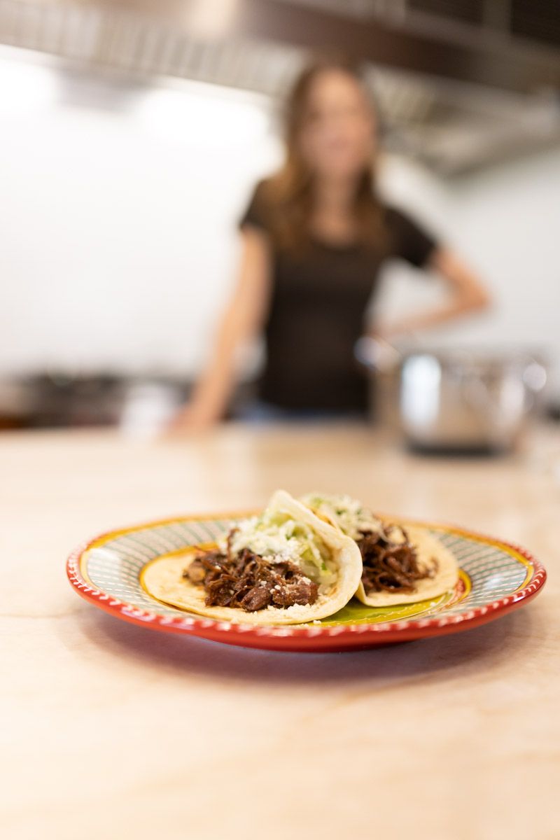 Tacos with shredded meat and cabbage served on decorative plate with blurred kitchen background.